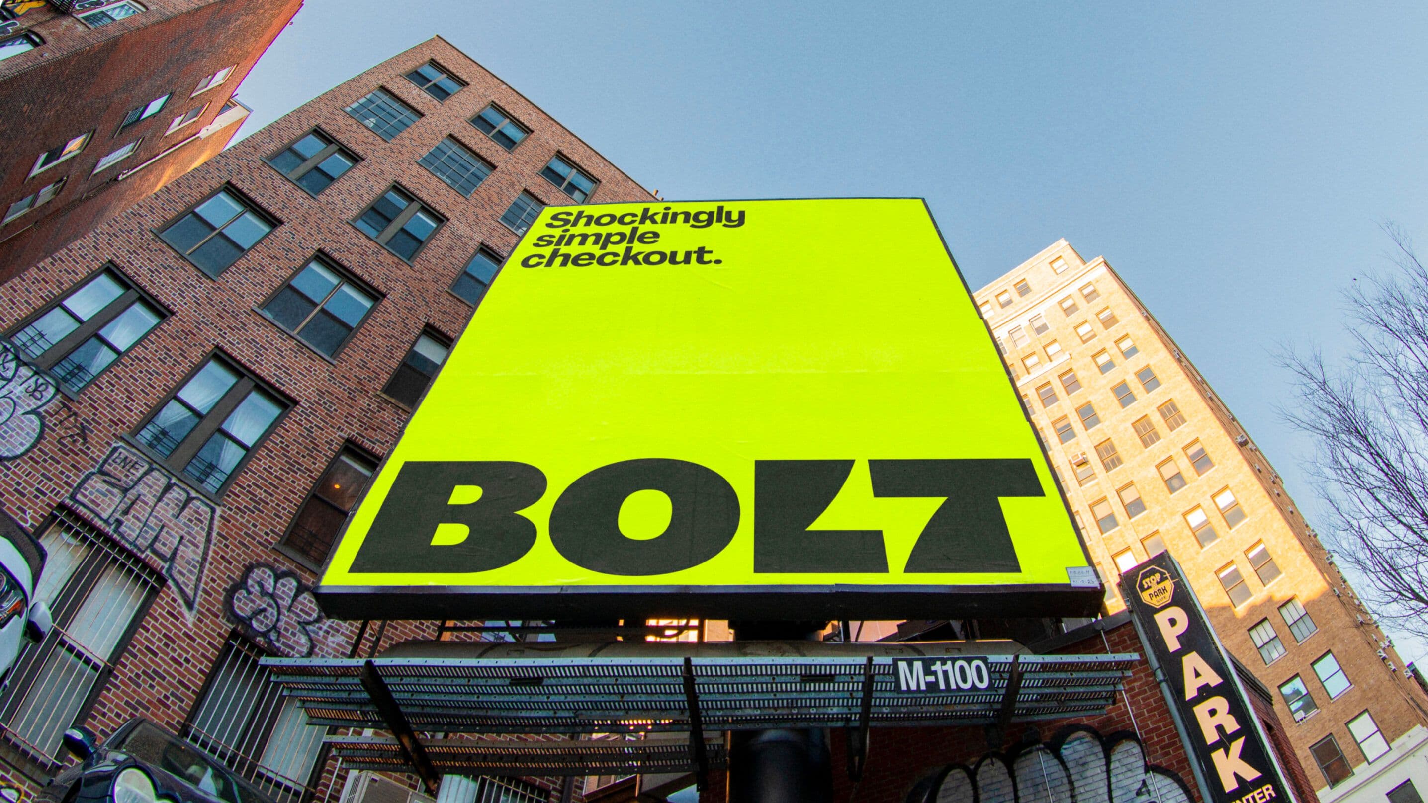 A large yellow billboard on a city street reads, “Shockingly simple checkout.” in smaller black text, and “BOLT” in bold black letters, mounted against tall brick buildings with graffiti.