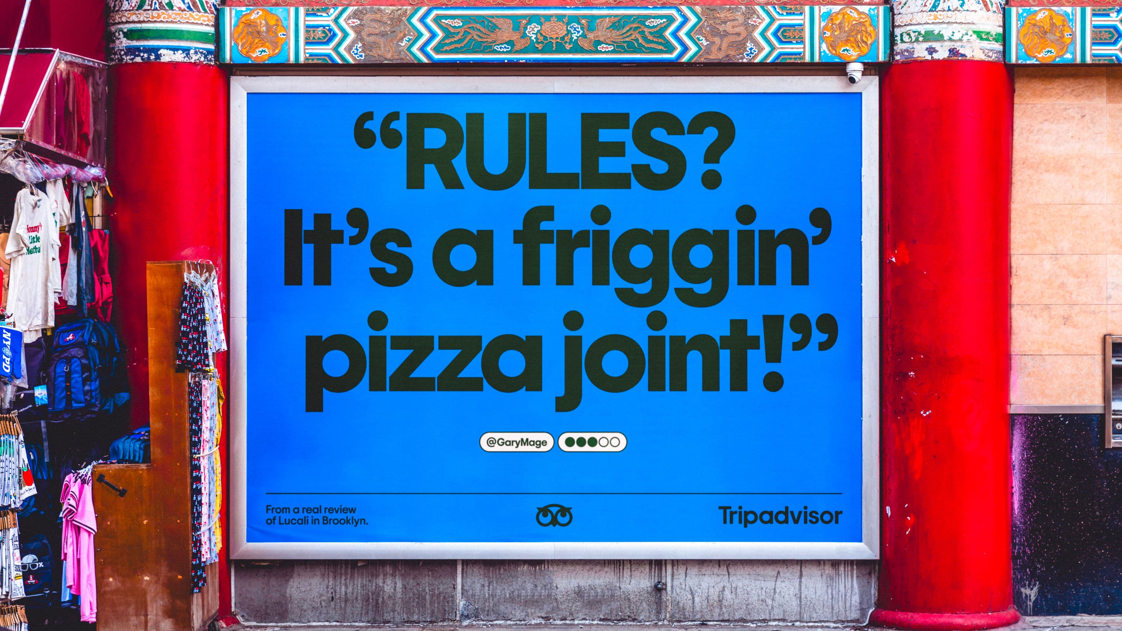 A blue billboard on a street reads: RULES? Its a friggin pizza joint! with attribution to a TripAdvisor review, surrounded by red columns and ornate decorative trim.