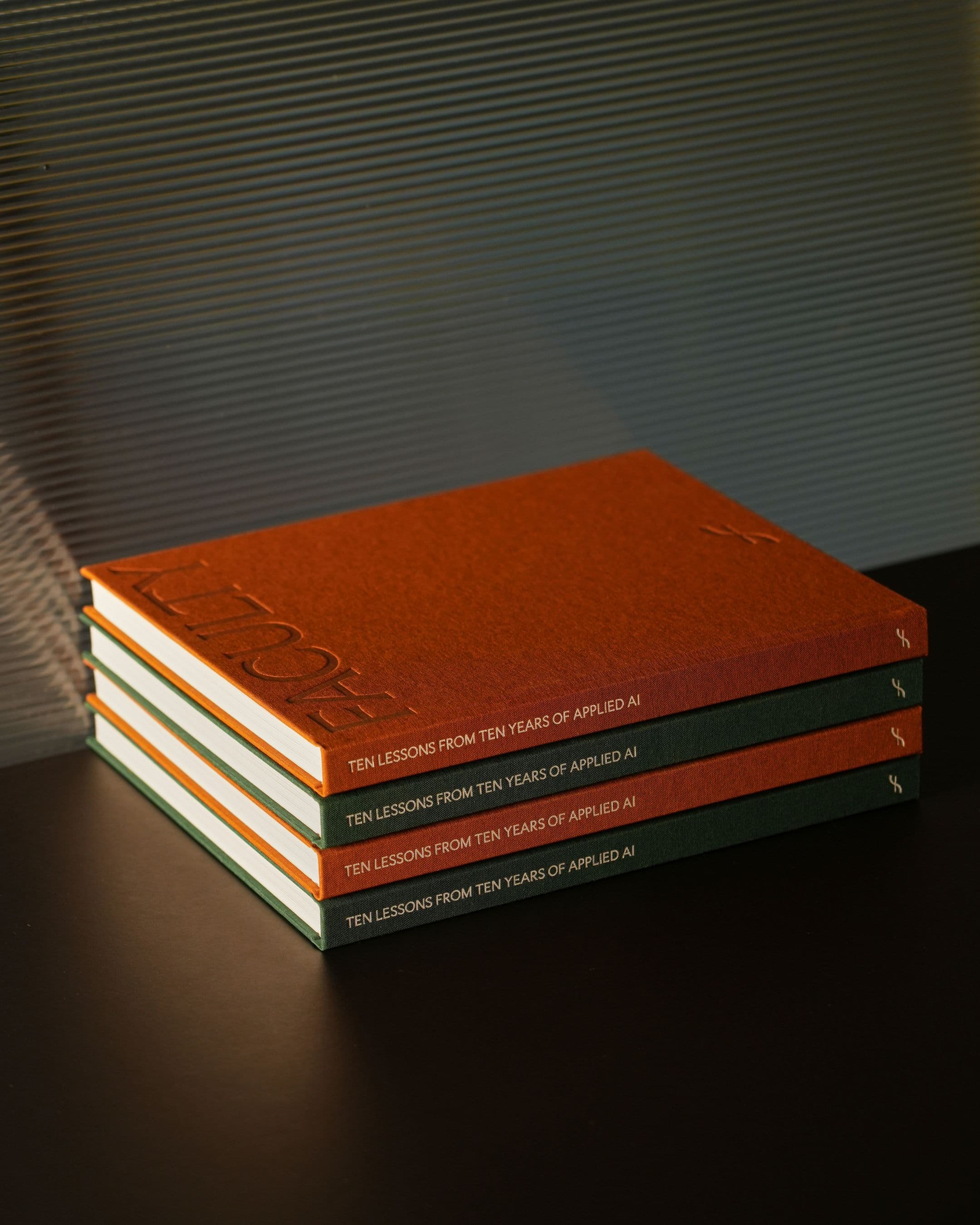 Four hardcover Faculty branded books with orange covers and green spines are stacked on a table.