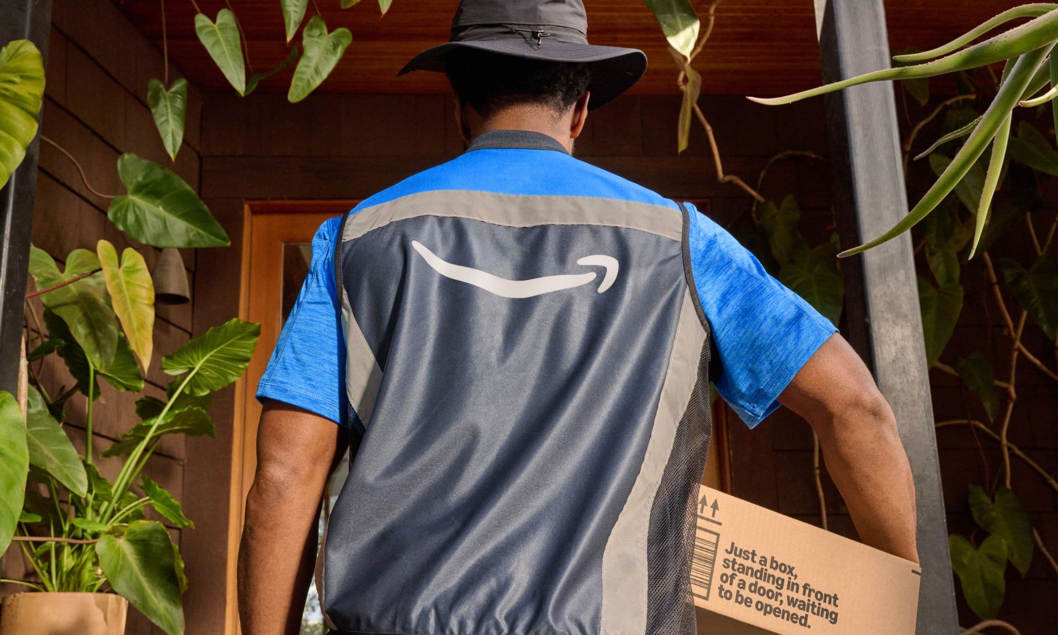 A man in amazon vest carrying a delivery package.