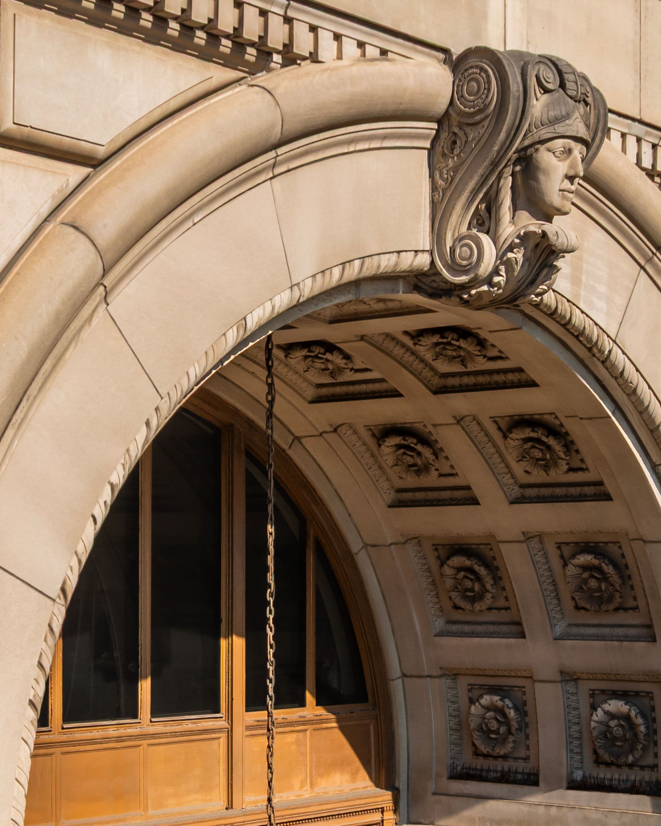 Close-up of a stone archway with an ornate carved classical face wearing a helmet.