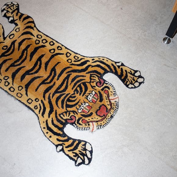A rug designed to look like a cartoon tiger with orange and black stripes is laid on a light-colored floor, partially visible in the corner of a room.