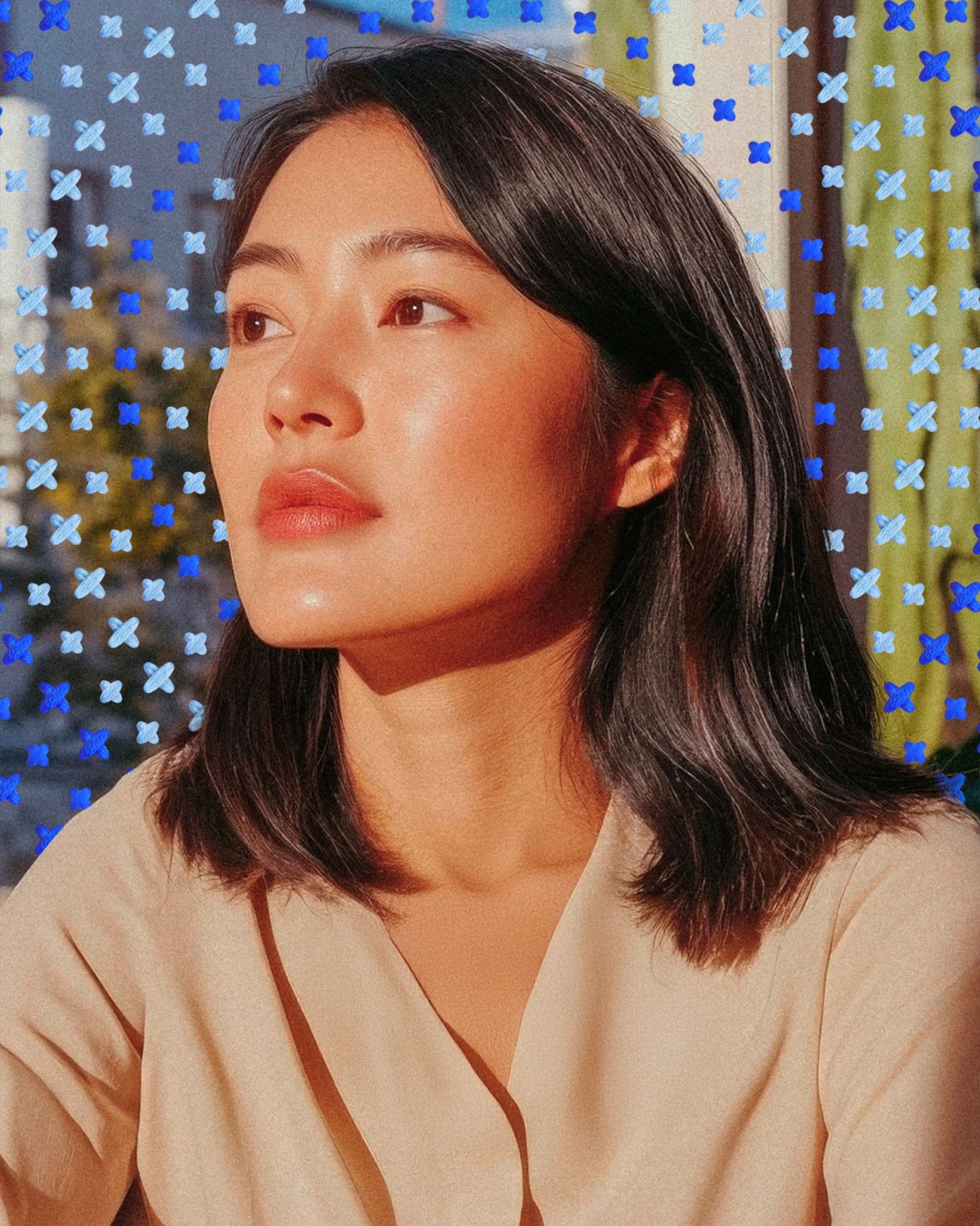 A woman with straight dark hair looks thoughtfully to the side surrounding her are a pattern of blue, white, and purple X marks.