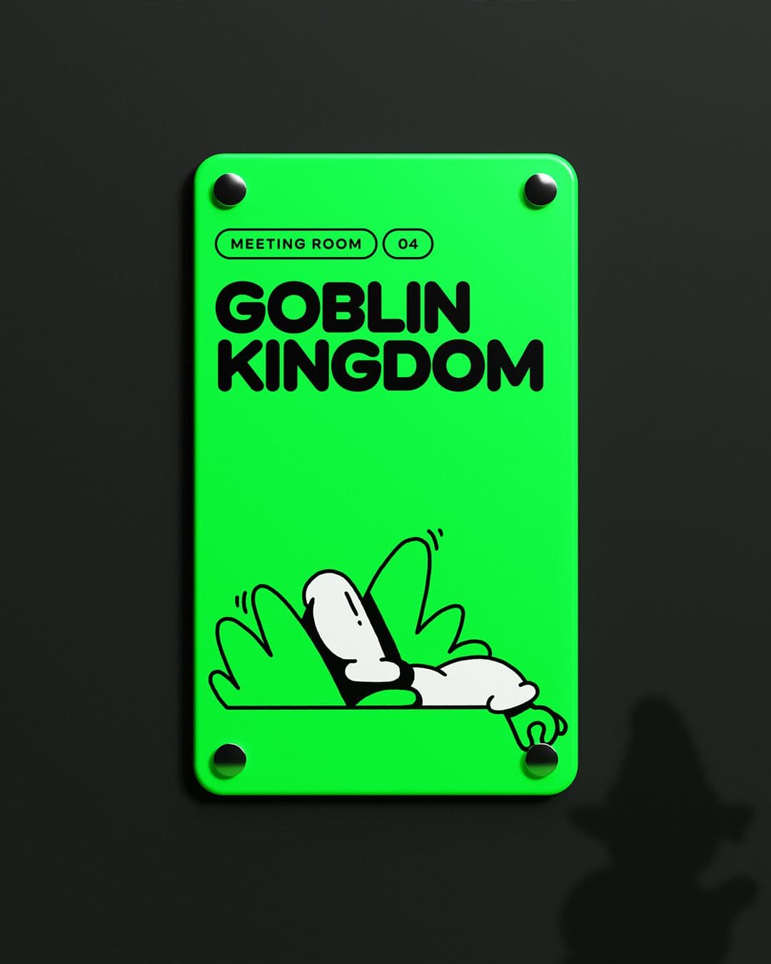 A bright green meeting room sign. The room is called the 'Goblin Kingdom'. The Marblex mascot is reaching for one of the circular pins of the sign as if it was a coin.