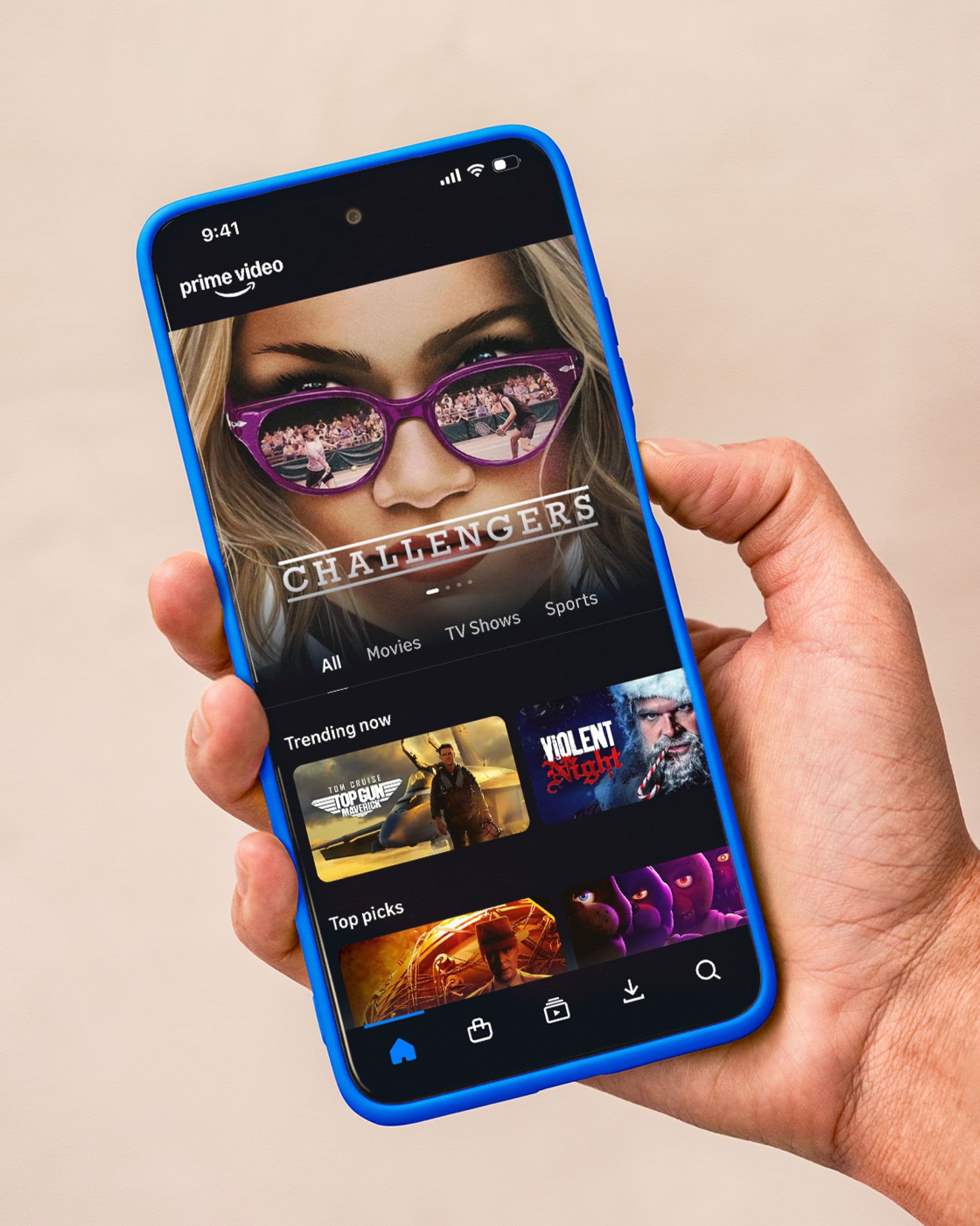 A hand holds a smartphone displaying the Prime Video app. The screen shows the movie Challengers at the top, with sections for Trending now and Top picks below it.