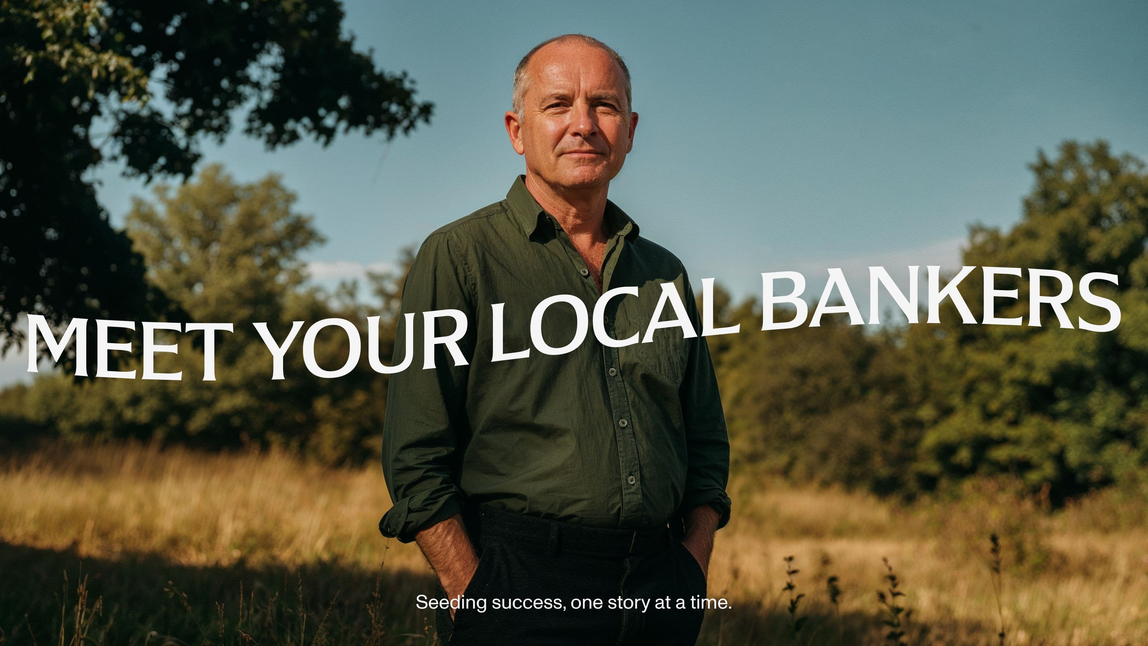 A middle-aged man stands in a grassy field with trees behind him, wearing a green shirt and looking at the camera. Overlaid text reads, “MEET YOUR LOCAL BANKERS.” Smaller text below says, “Seeding success, one story at a time.”.