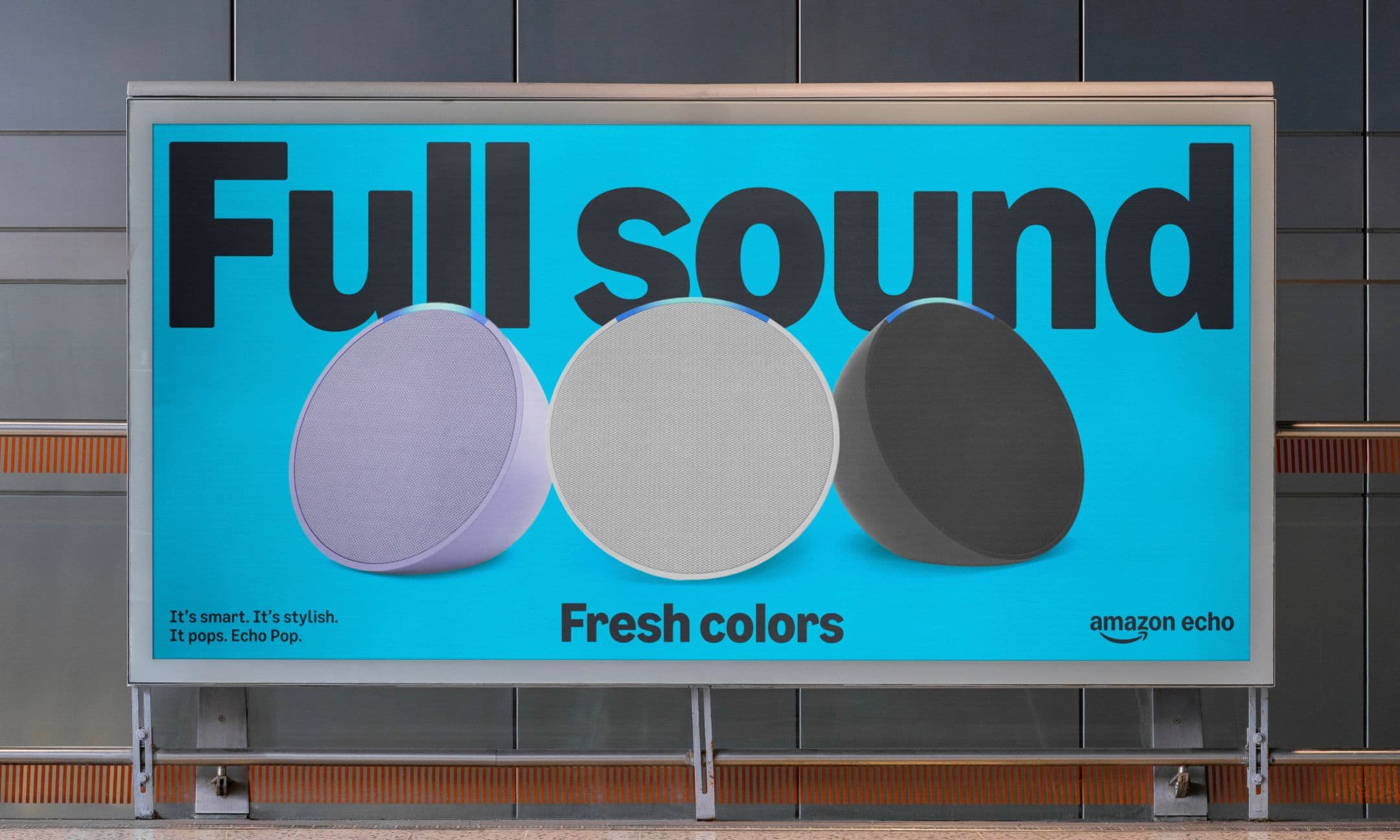 A billboard advertises Amazon Echo Pop speakers in three colors against a bright blue background with the words “Full sound” in large text and “Fresh colors” and the Amazon Echo logo below.