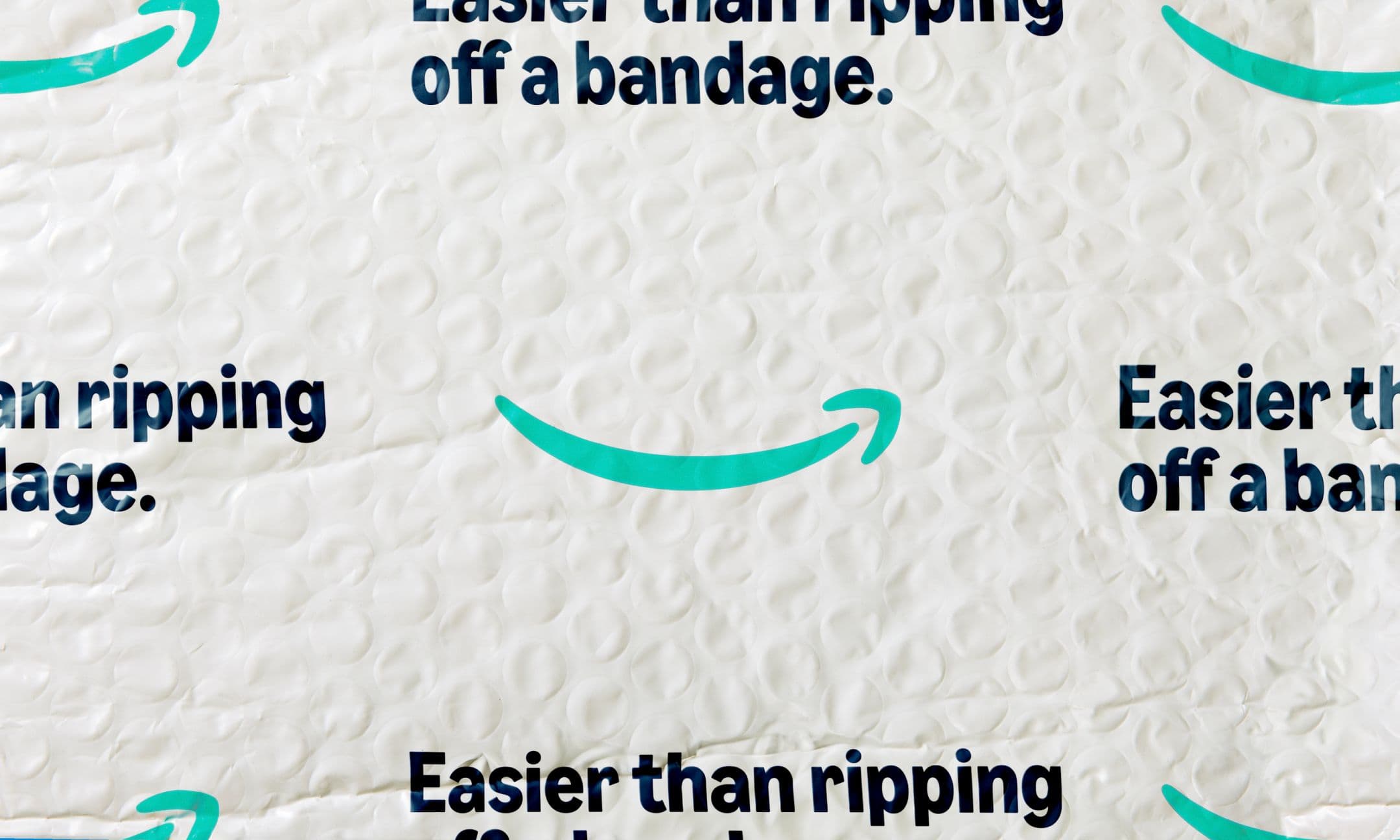 A padded white Amazon mailer with the Amazon smile logo and the text Easier than ripping off a bandage printed repeatedly in bold black letters.