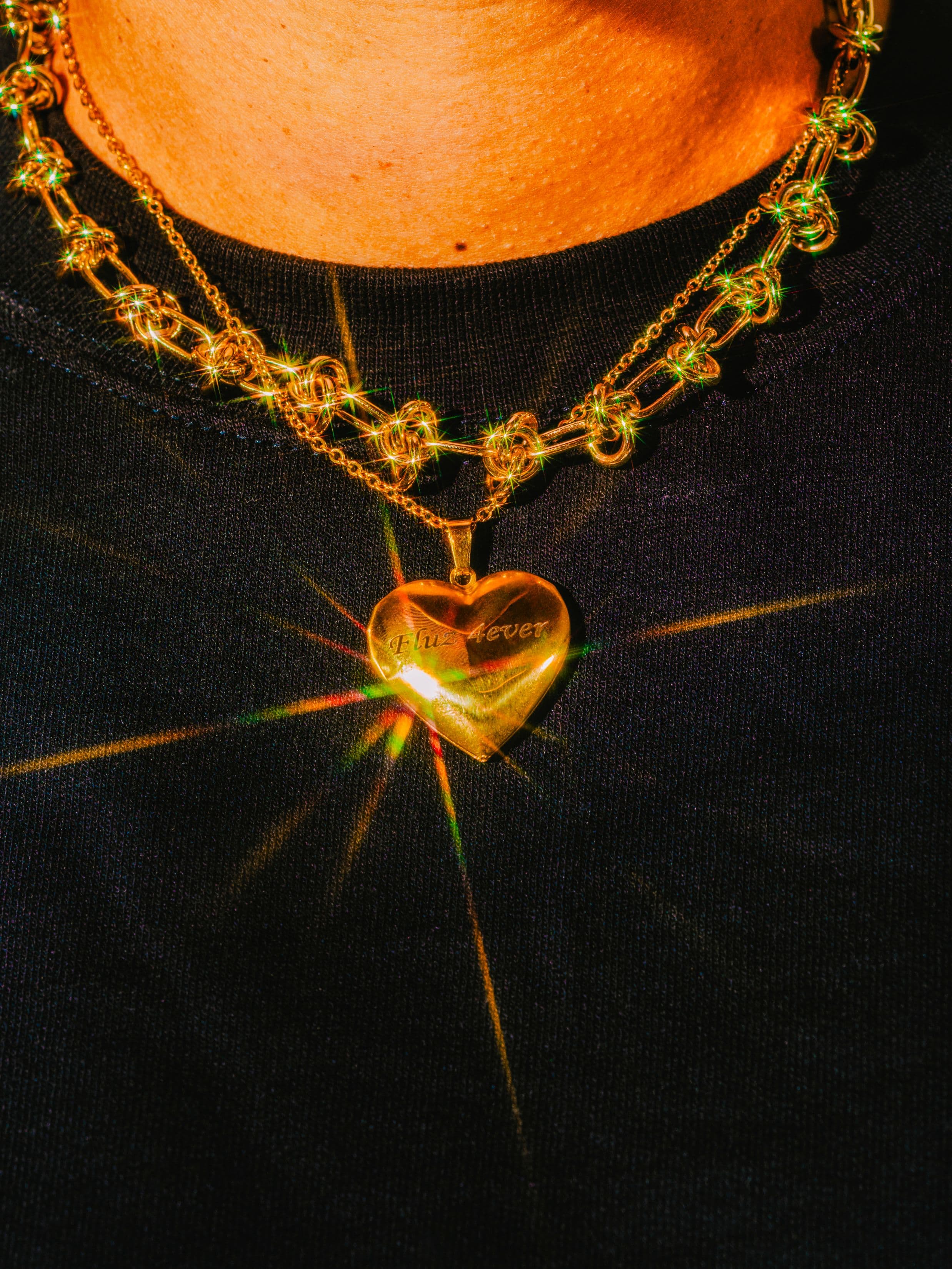 A close-up of a gold heart-shaped locket necklace with Yours Forever engraved on it, worn over a dark shirt.