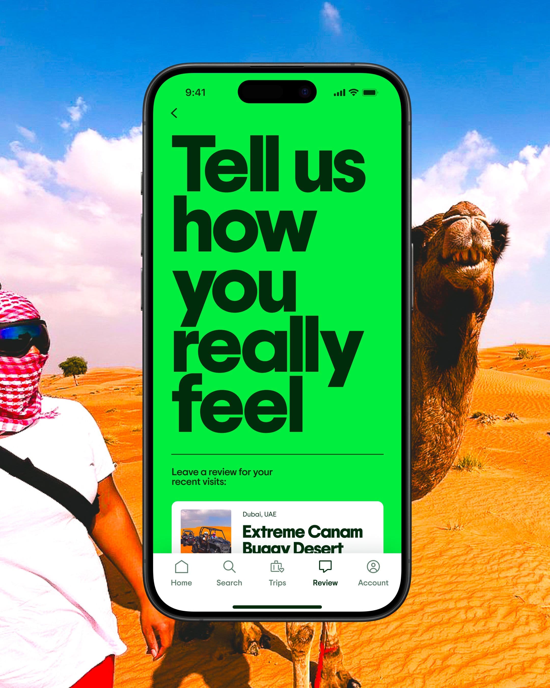 A smartphone displaying a bright green review screen with the text "Tell us how you really feel" is shown in front of a desert scene with a person in a headscarf and sunglasses beside a smiling camel.