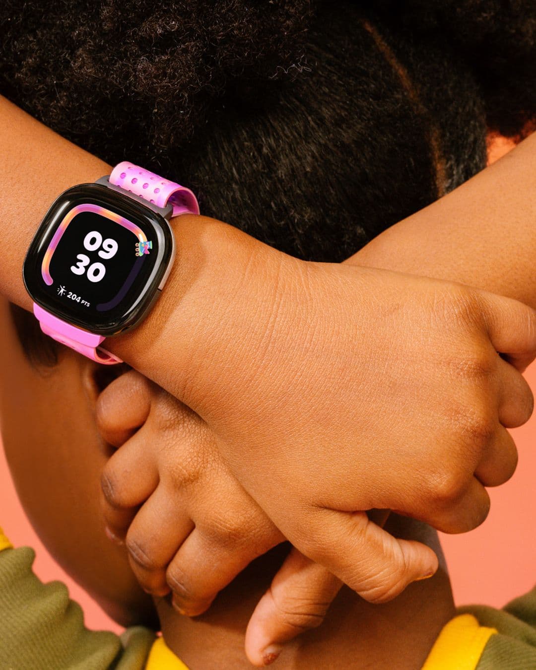 A child with arms crossed behind their head wears a purple FItbit Ace watch displaying their steps count.