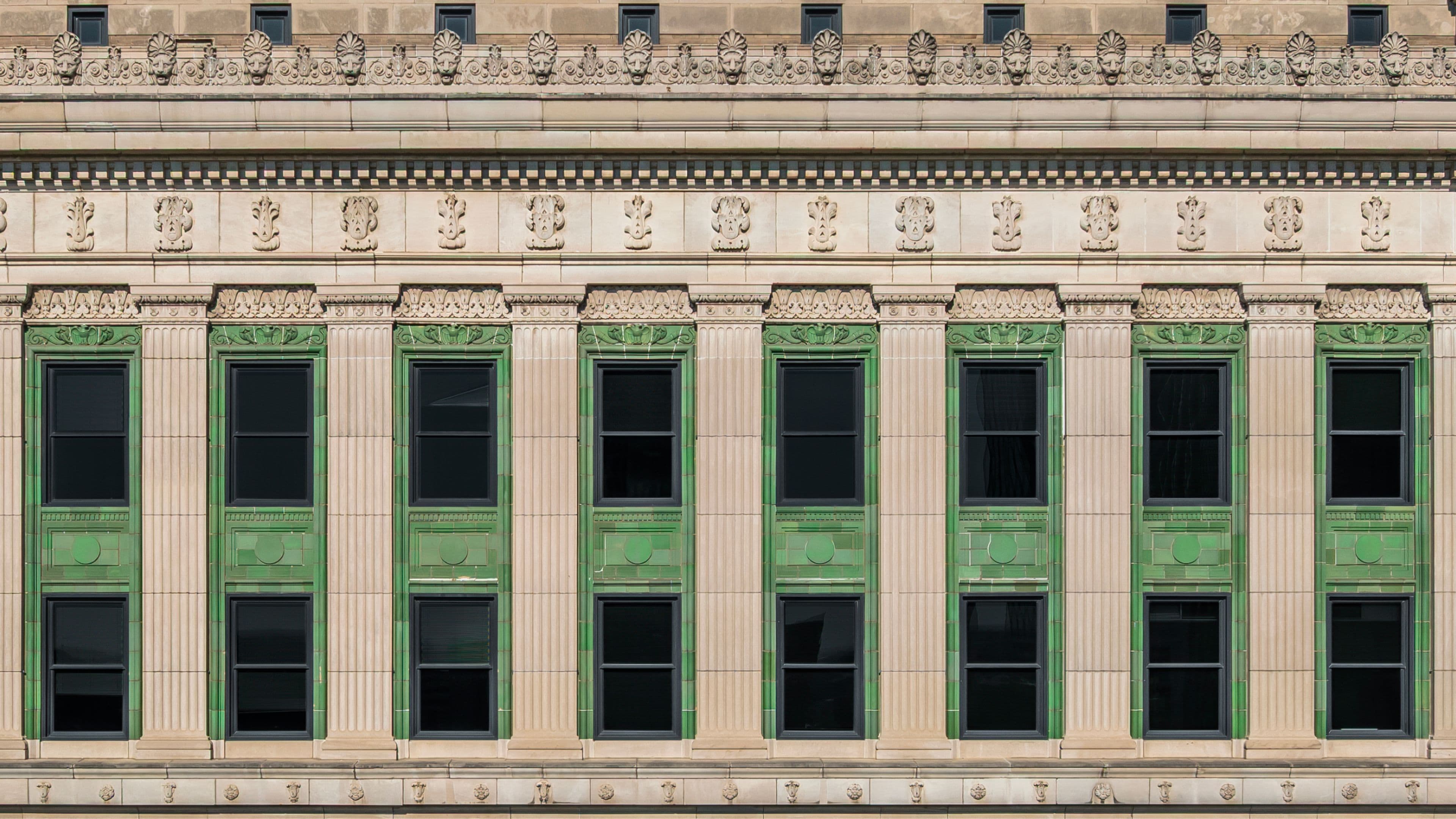 A symmetrical building facade with tall green-framed windows with decorative columns.