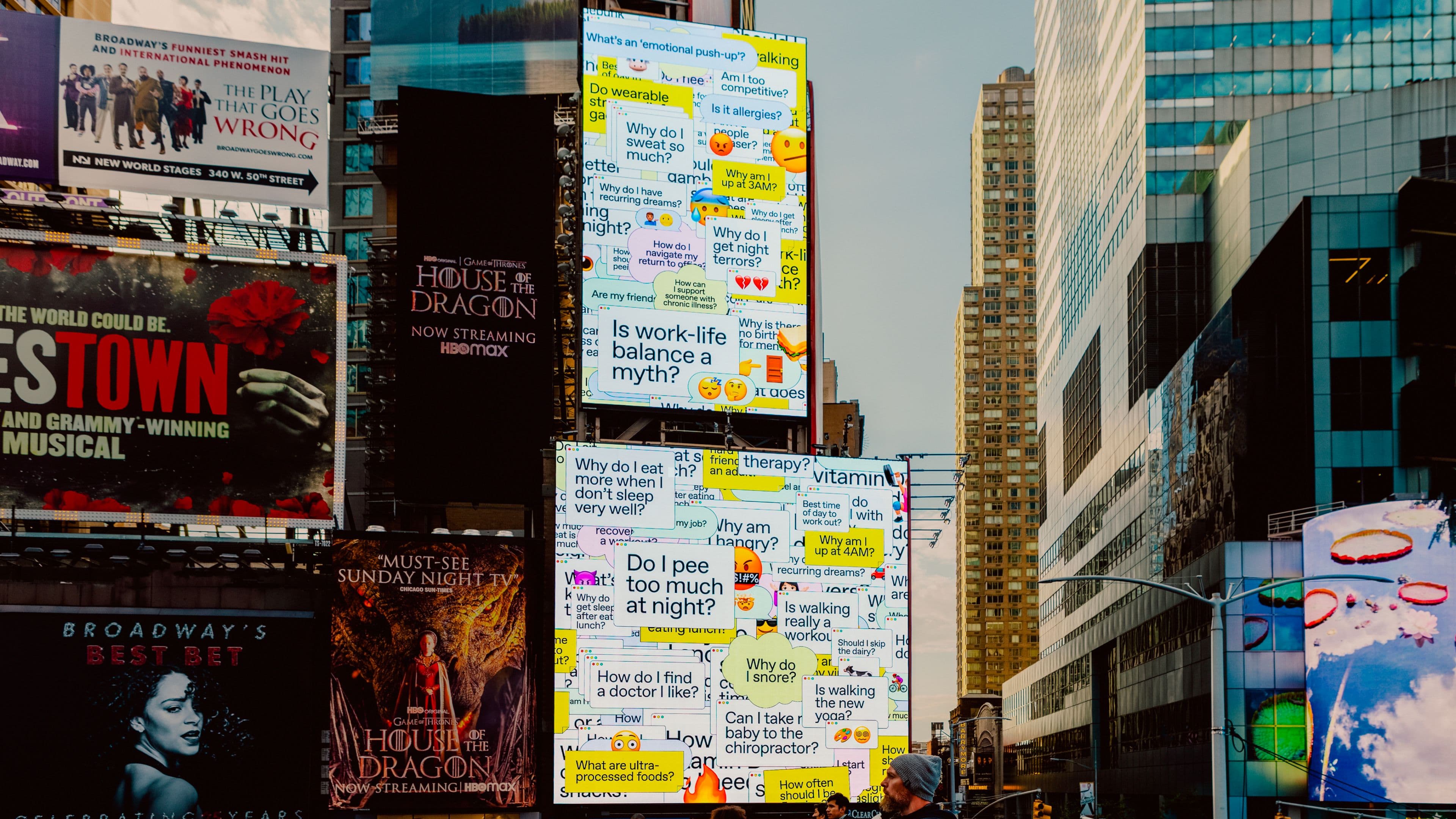 Bright digital billboards in Times Square display colorful text boxes with mental health questions.