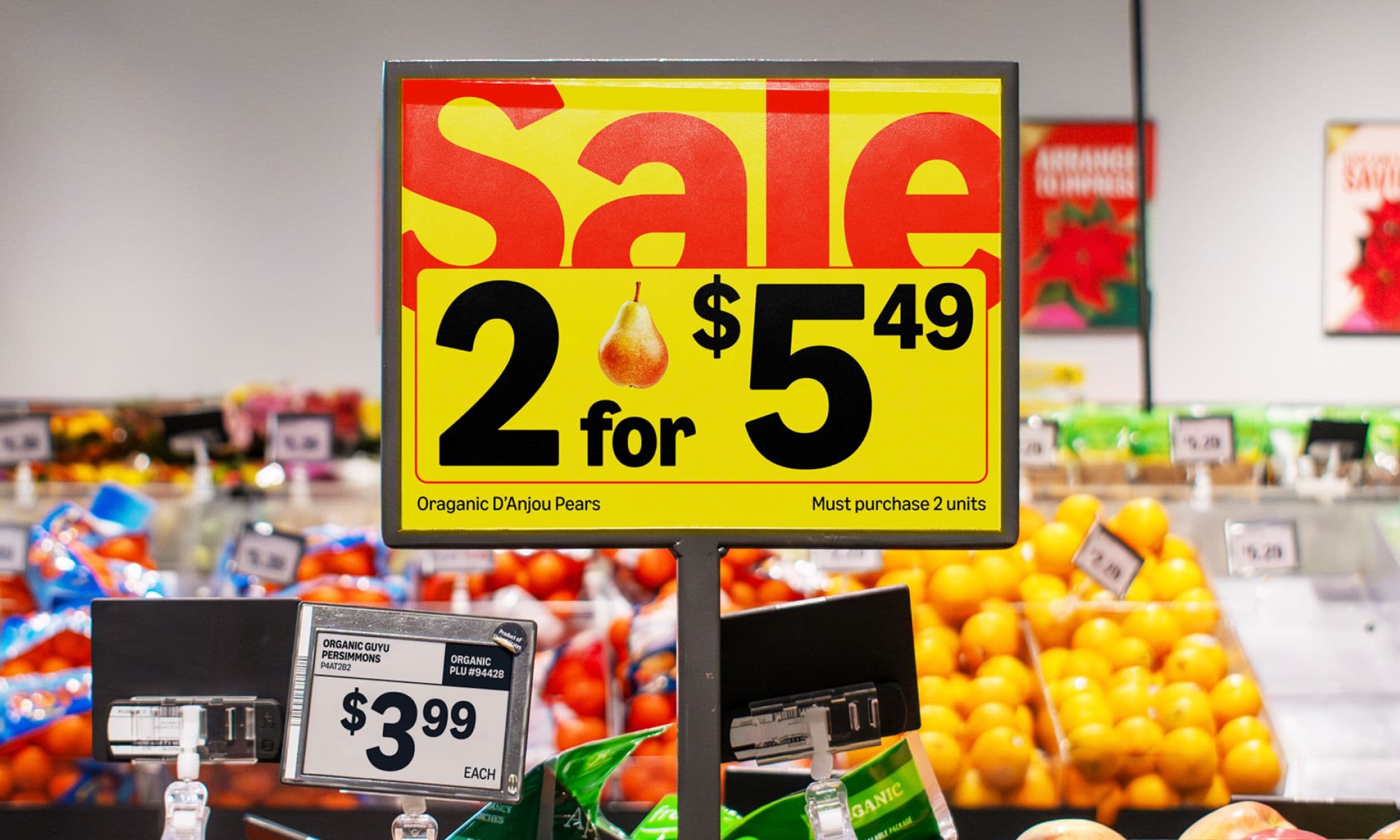 A yellow and red sale sign in a grocery store advertises organic D’Anjou pears at 2 for $5.49.