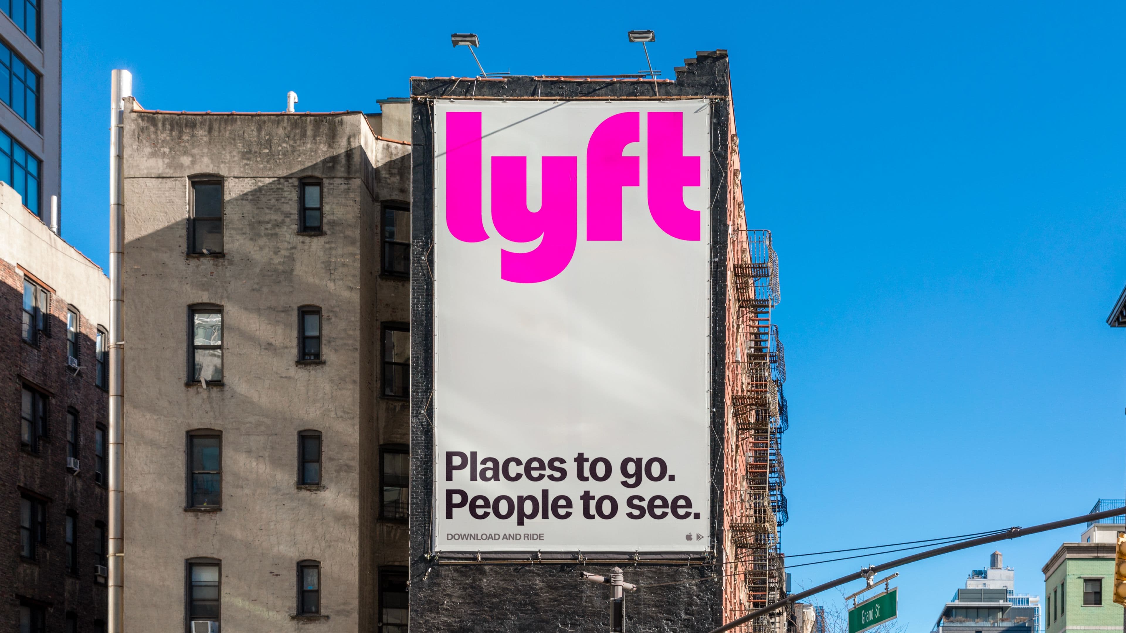 A large Lyft billboard on the side of a city building displays the pink Lyft logo and the text "Places to go. People to see." against a clear blue sky.