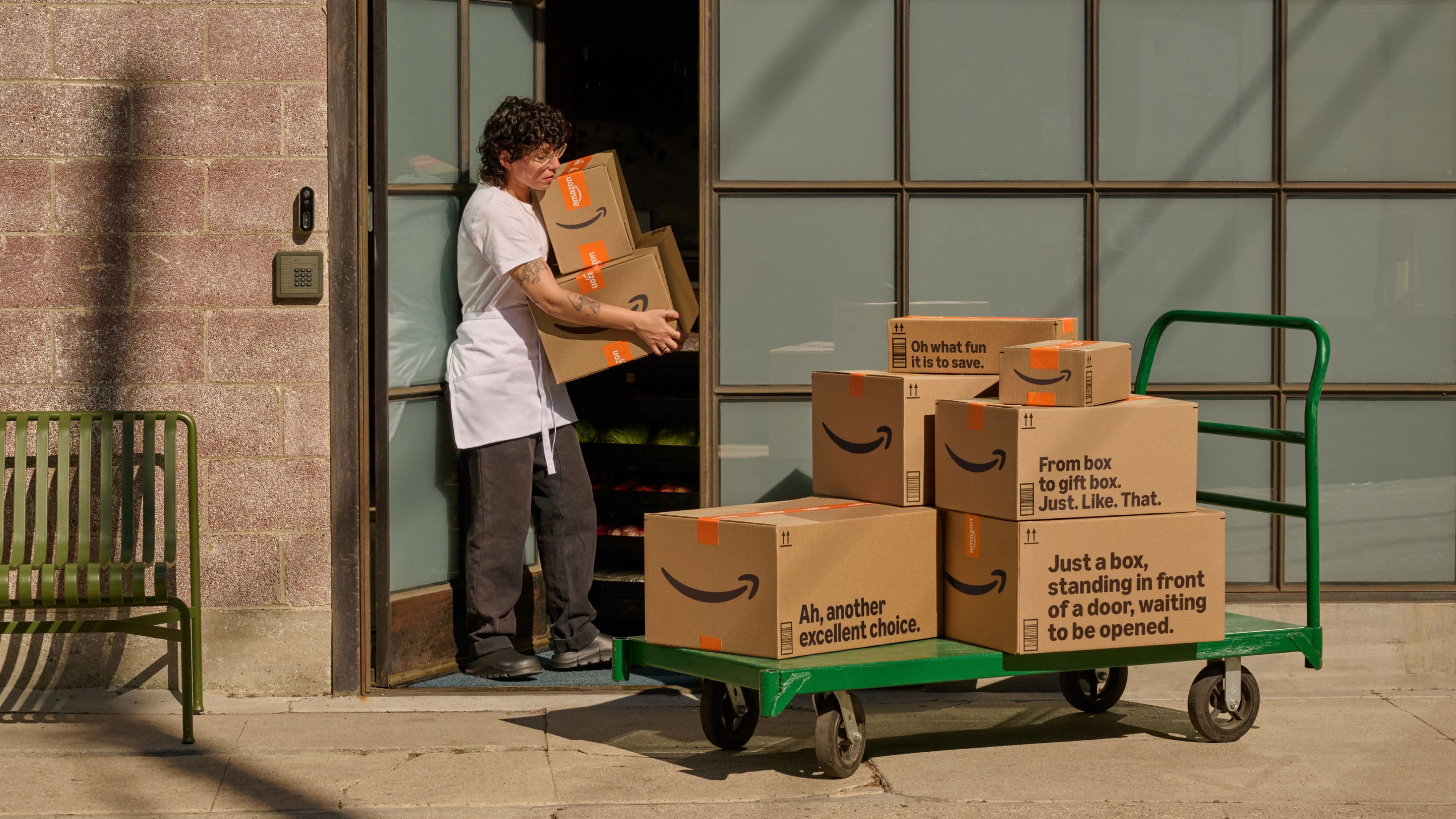 Person moving Amazon packages onto a cart outside a building.